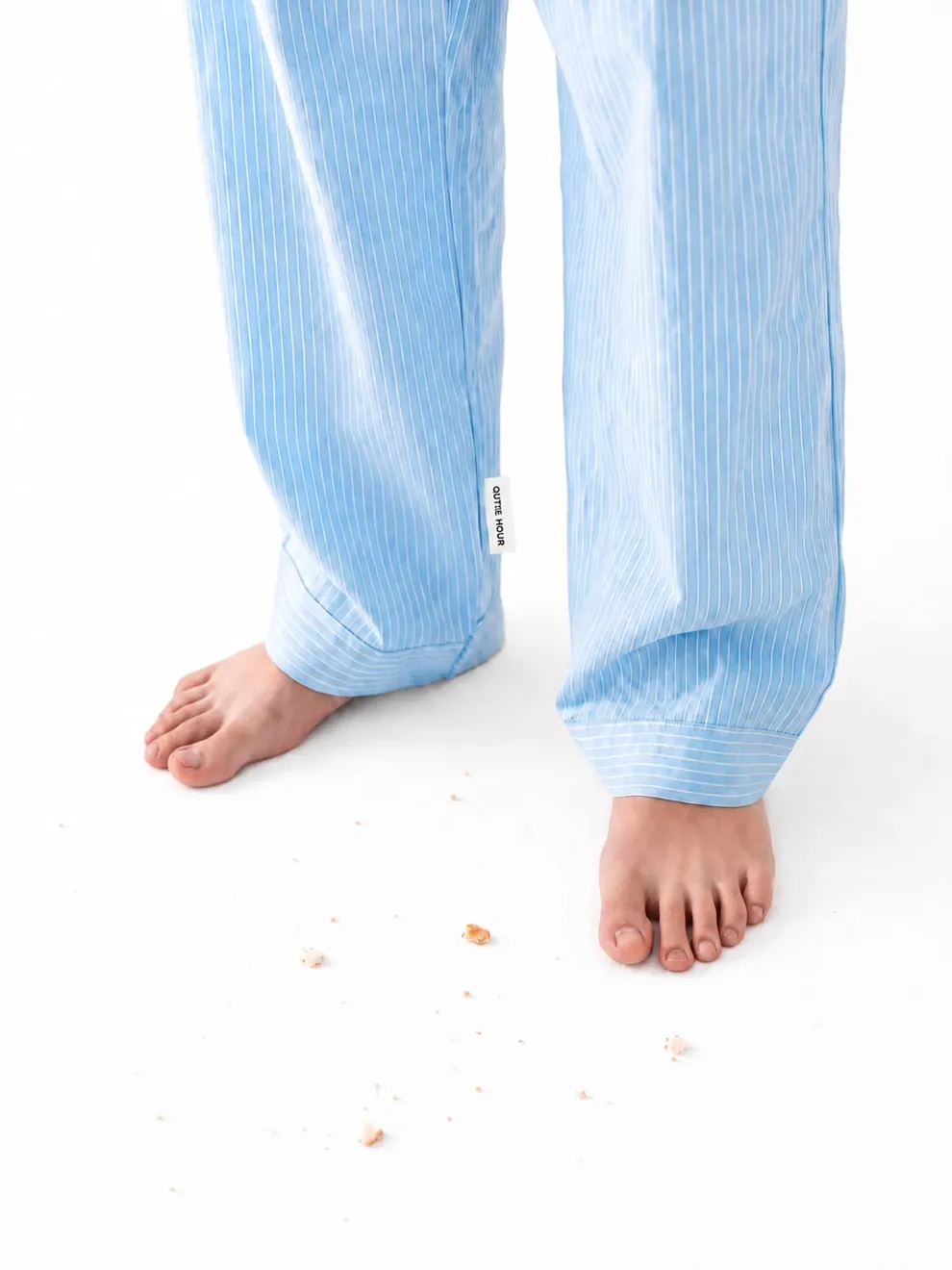QUIET HOUR — bare feet in soft blue pajamas with crumbs on white floor, quiet unhurried morning mood
