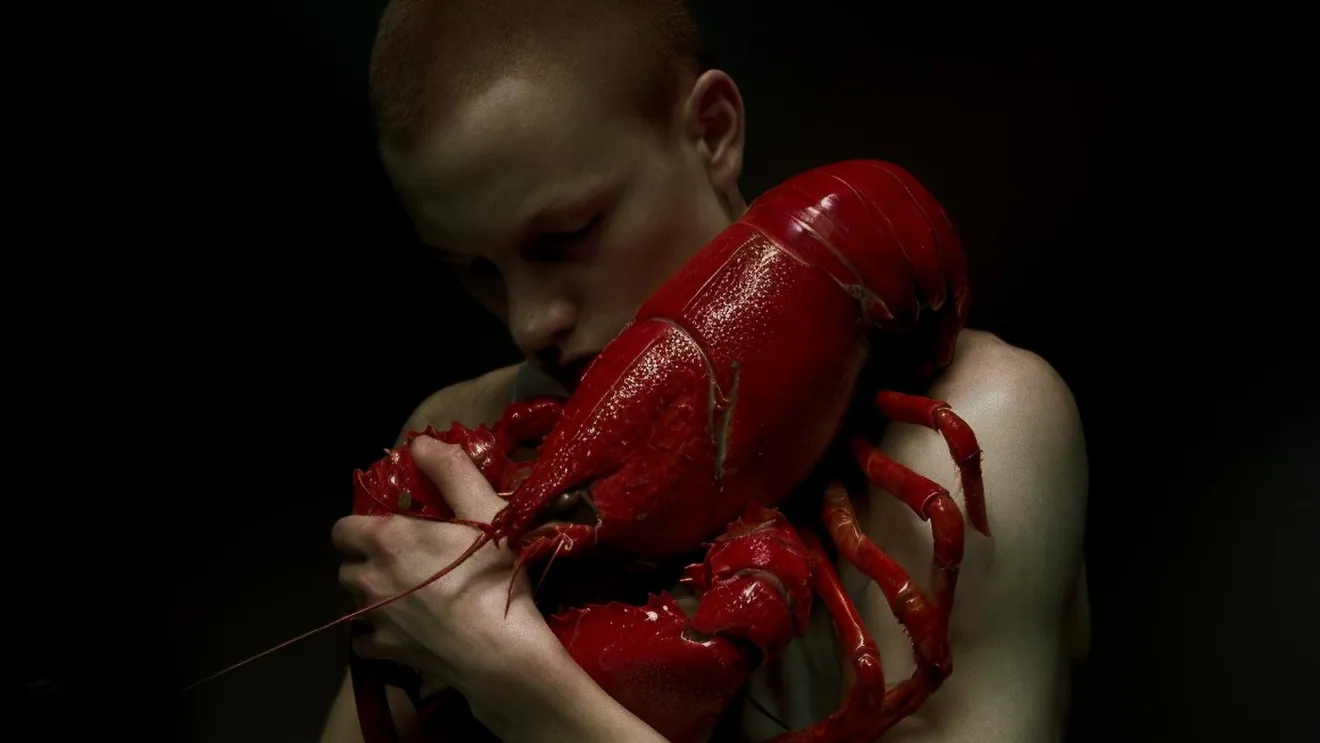 OCEVIA ORIGIN — person holding a red lobster against bare skin in a dark, editorial seafood brand portrait