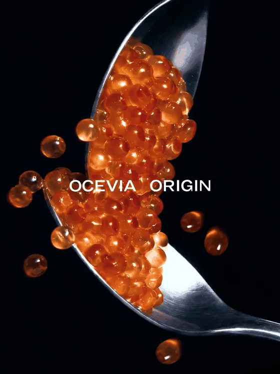 OCEVIA ORIGIN salmon roe served on a spoon against black, with the brand mark set across the caviar